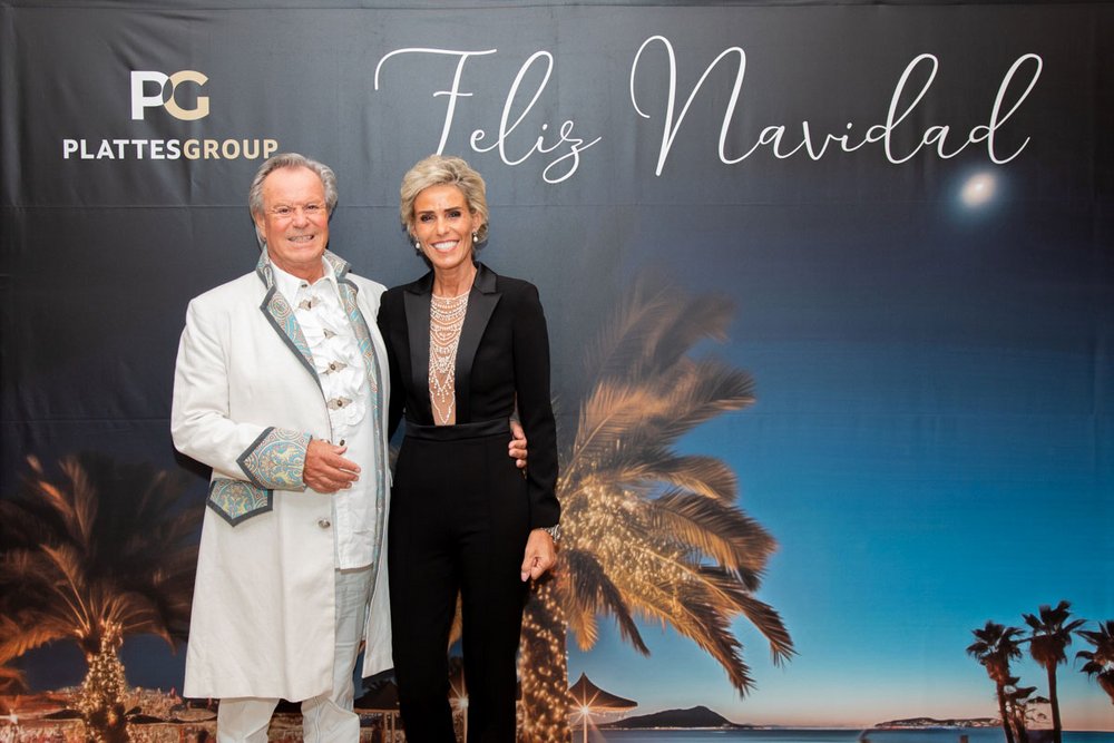 Die Geschäftsführer der PlattesGroup, Willi und Yvonne Plattes, stehen in festlicher Kleidung vor einen Fotowand dem Schriftzug "Feliz Navidad" mit einem Logo des Unternehmens